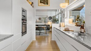 A modern kitchen with white cabinetry, a built-in oven, a large island with a sink, and a dining area with a table and chairs. - 3 bedroom beautiful home in Nibe (Nibe)