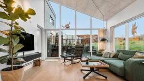A spacious living room with a large TV, comfortable seating, a dining area, and large windows offering a view of the outdoors. - 3 bedroom beautiful home in Nibe (Nibe)