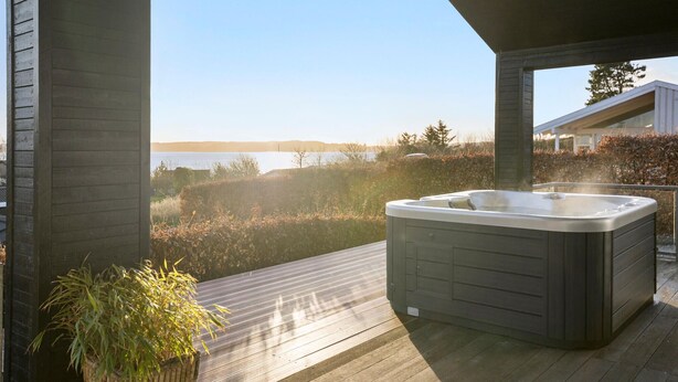 A hot tub on a wooden deck with a view of a lake and distant hills. - 3 bedroom beautiful home in Nibe (Nibe)