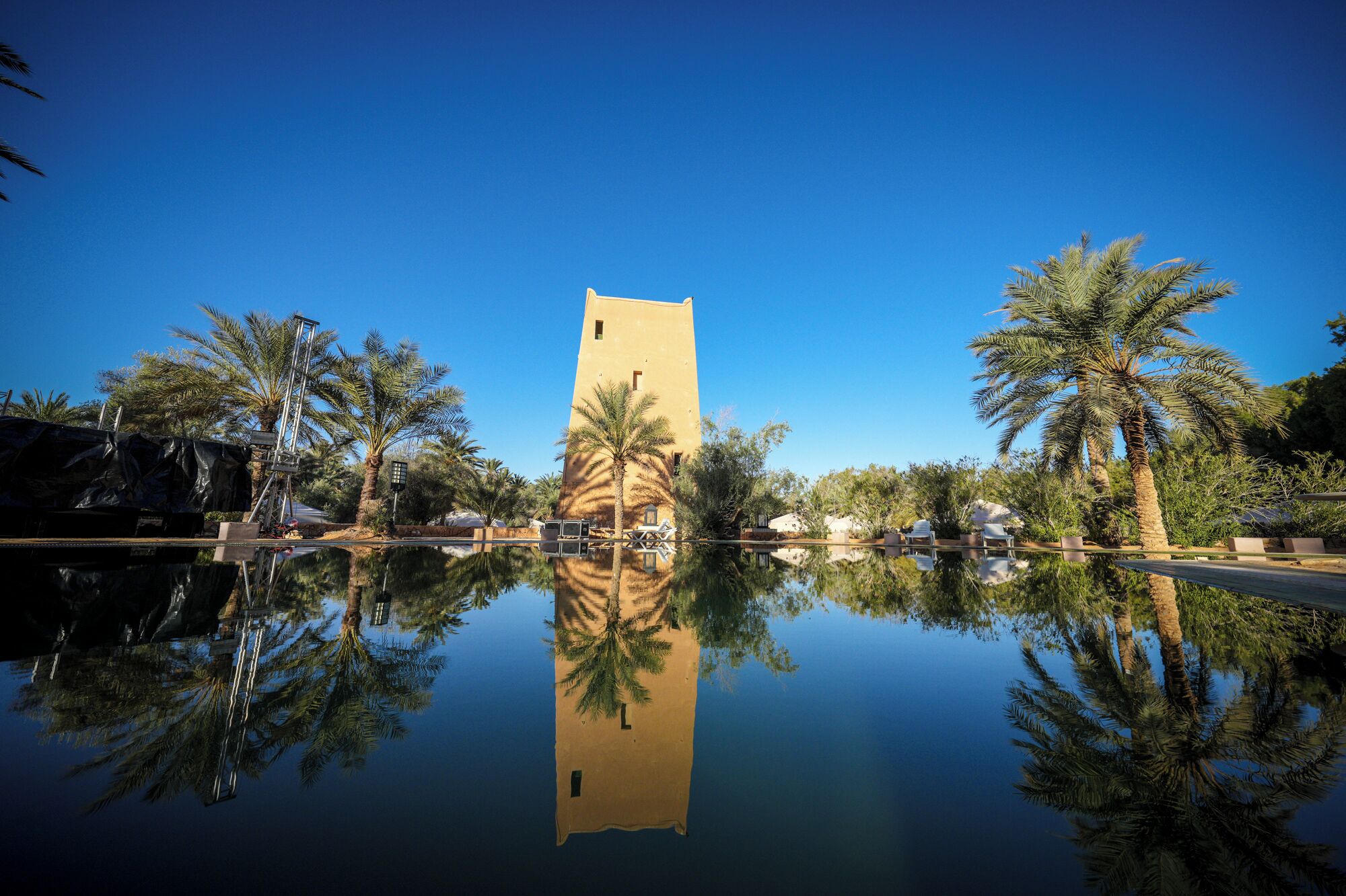 A building with a tower, surrounded by palm trees and a reflective pool.