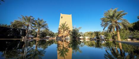 A building with a tower, surrounded by palm trees and a reflective pool.