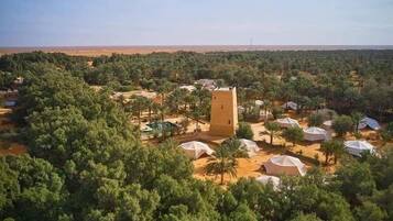 An aerial view of a resort with multiple dome-shaped tents, a central tower, and dense surrounding greenery.