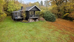 Une cabane avec une véranda, une cheminée et une petite terrasse.