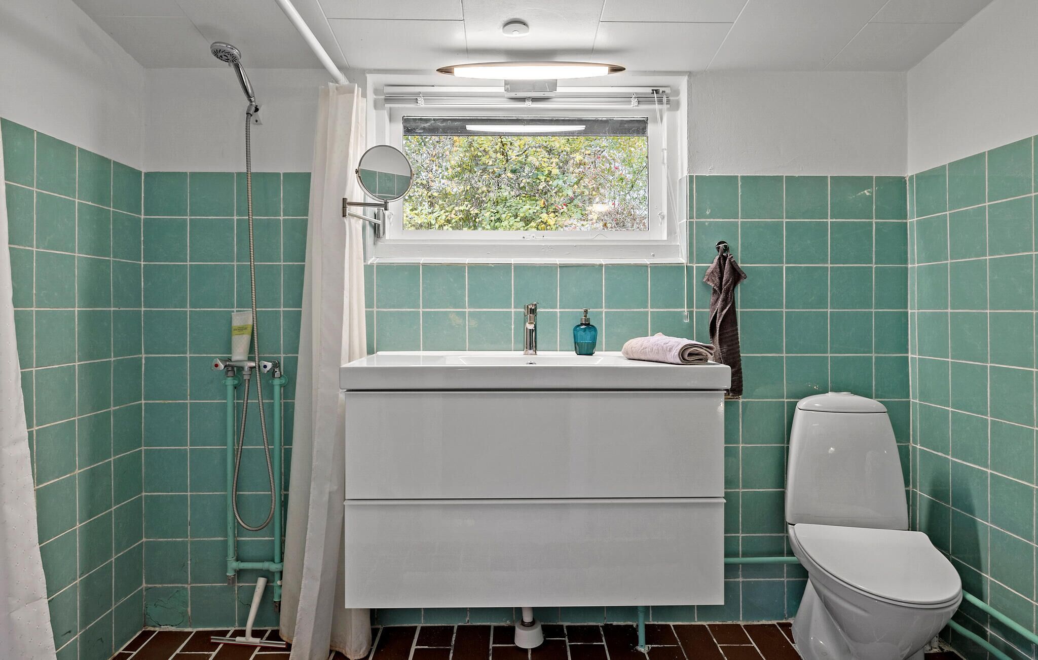Een badkamer met raam, wastafel, toilet en douche.