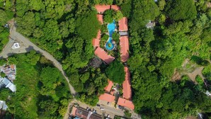 Luchtbeeld van een resort met een zwembad, omringd door weelderige begroeiing en gebouwen met rode daken.