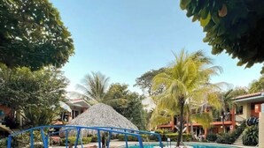 Une piscine avec un pont, entourée de palmiers et bordée d’un bâtiment doté de balcons.