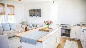 Eine moderne Küche mit weißen Schränken, einer Holz Arbeitsplatte und einem eingebauten Backofen. Es gibt einen Essbereich mit einem hellblauen Teppich und einem Holztisch.