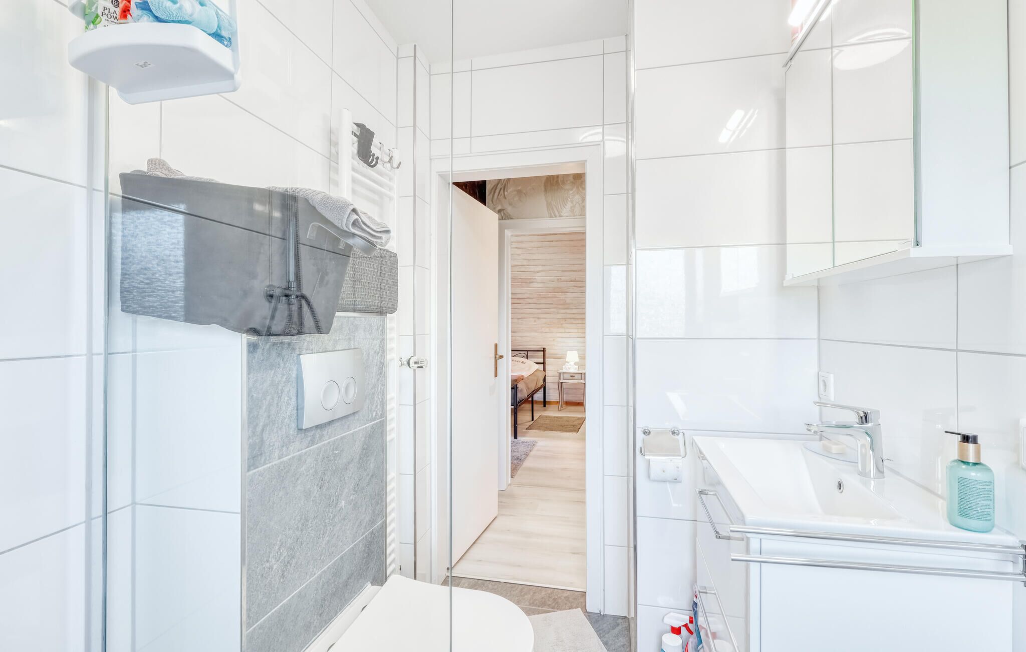 Een moderne badkamer met een glazen douchecabine, een witte wastafel en een wastafelmeubel met een spiegel.