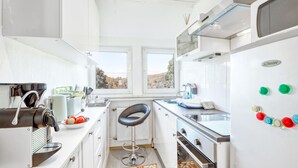A compact kitchen with a coffee maker, a bowl of fruit, a sink, and a window with a view of trees.