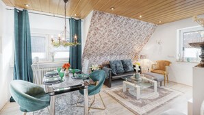 A modern living room with a dining area, featuring a wooden ceiling, a patterned wall, and a cozy seating arrangement.