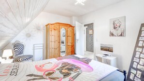 A bedroom with a bed, a wooden wardrobe, a desk with a computer, and wall decorations.