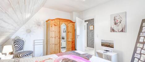 A bedroom with a bed, a wooden wardrobe, a desk with a computer, and wall decorations.