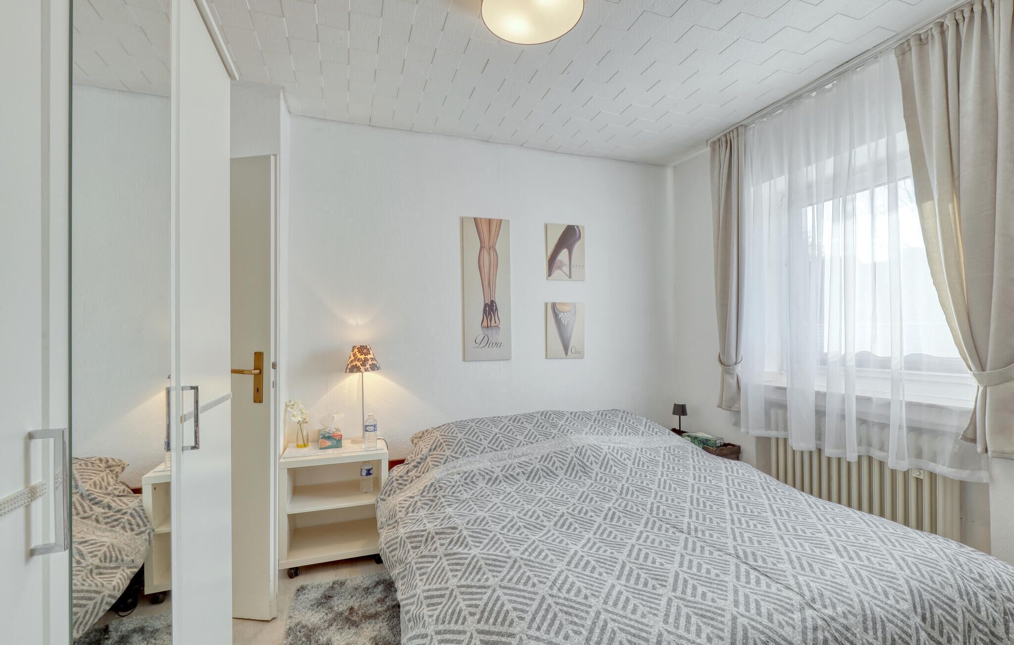 Un dormitorio con una colcha estampada, una lámpara de noche, una mesita de noche y dos cuadros en la pared.