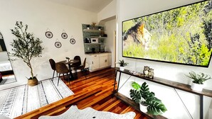 Een moderne woonkamer met houten vloer, een eethoek, een keuken en een grote televisie waarop een natuurscène wordt getoond.