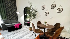 Een moderne woonkamer met een grijze bank, een ronde eettafel met stoelen, een patroonrijk tapijt en een potplant.