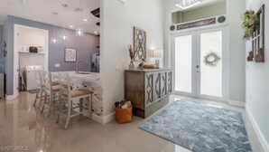 Amplia sala de estar con una mesa de comedor, sillas, una cocina al fondo y un ventanal decorado con un adorno.