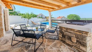 Un patio exterior con suelo de piedra, una piscina y una pérgola.
