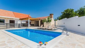 Una piscina con sillas de descanso, un porche cubierto y una terraza de piedra.