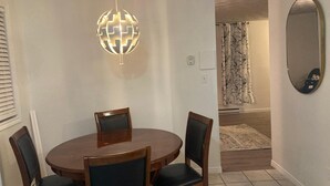 Un comedor con una mesa redonda de madera y cuatro sillas, una lámpara colgante y un espejo en la pared.
