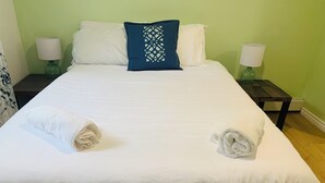 A neatly made bed with white linens, a blue decorative pillow, and two rolled towels on the bed. - Cozy basement place  (Kentville)