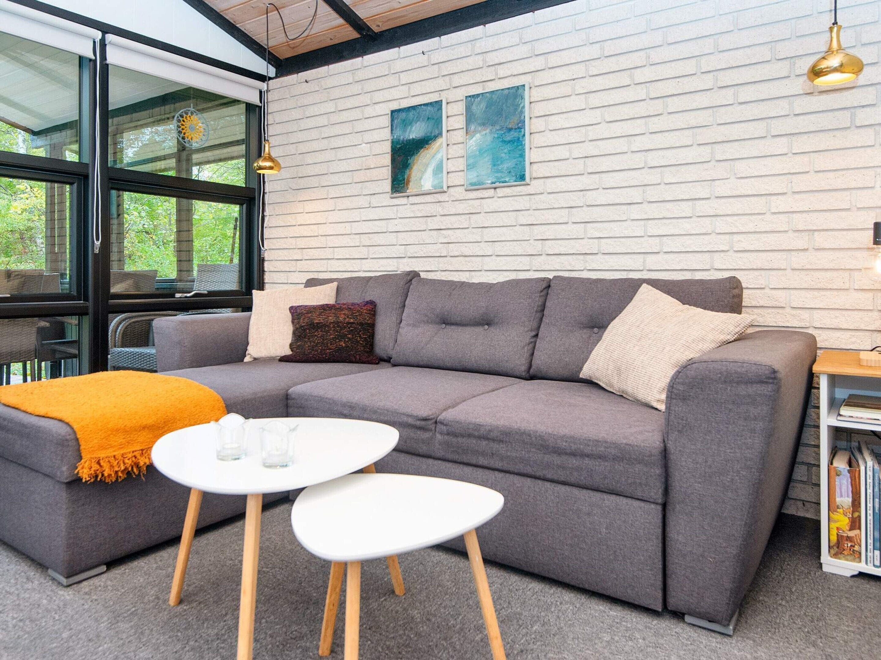 A modern living room with a grey sofa, two white tables, and a brick wall with artwork.