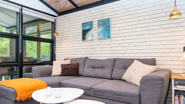 A modern living room with a grey sofa, two white tables, and a brick wall with artwork. - 4 Person Holiday Home in Farvang (Farvang)