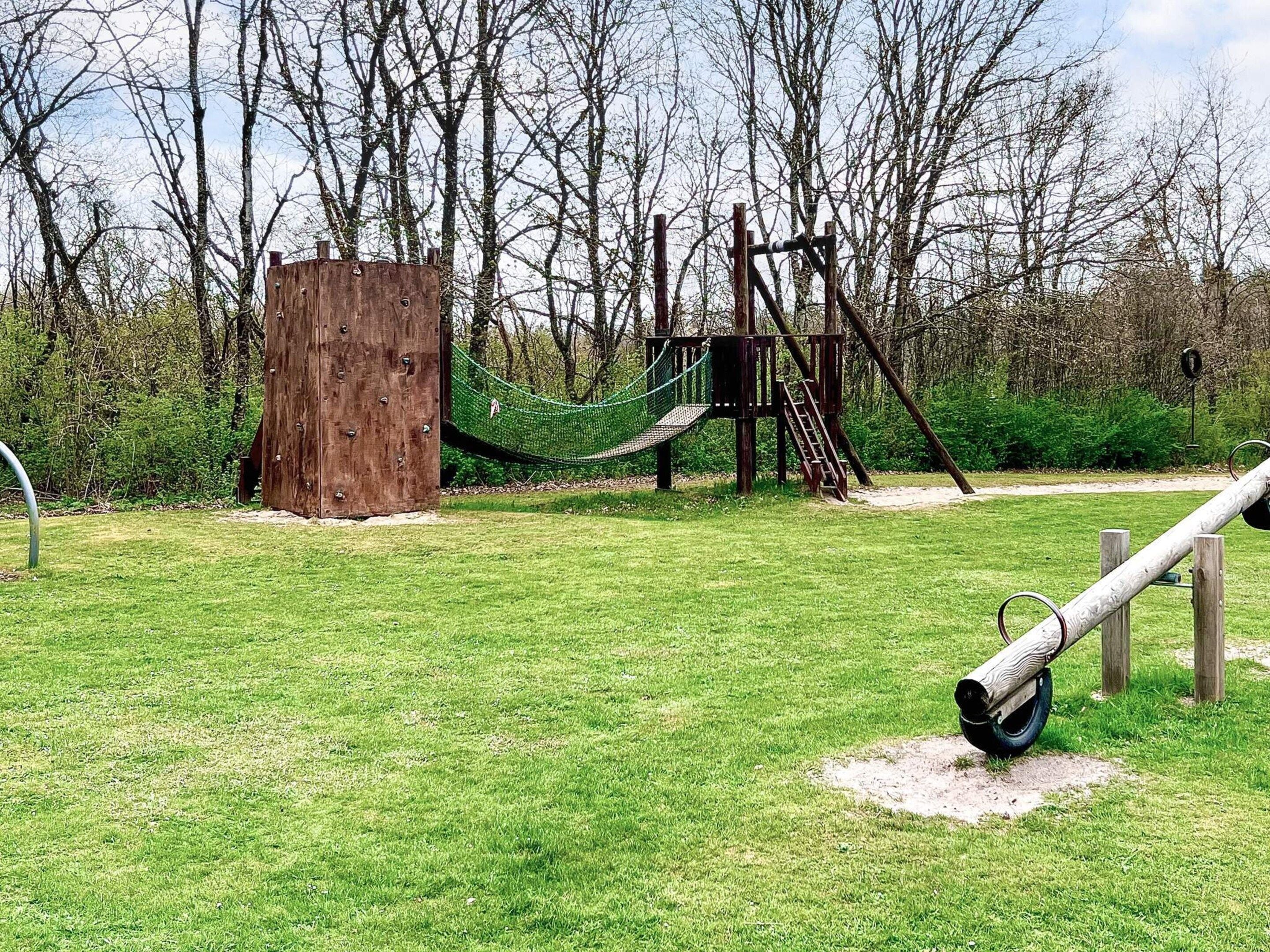 A playground with a wooden climbing structure, a rope net, and a tire swing.