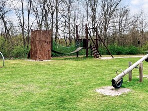 Un parque infantil con una estructura de madera para escalar, una red de cuerdas y un columpio de neumático.