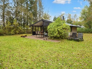 A covered outdoor area with a grill, chairs, and a small building. - 4 Person Holiday Home in Farvang (Farvang)