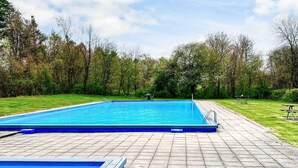 A rectangular swimming pool with a tiled deck, surrounded by a grassy area and trees.