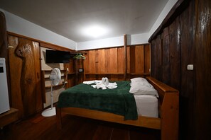 A wooden-framed room with a bed, a fan, and a television mounted on the wall.