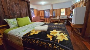 Una habitación con cama, un escritorio de madera, un refrigerador y una ventana con cortinas.
