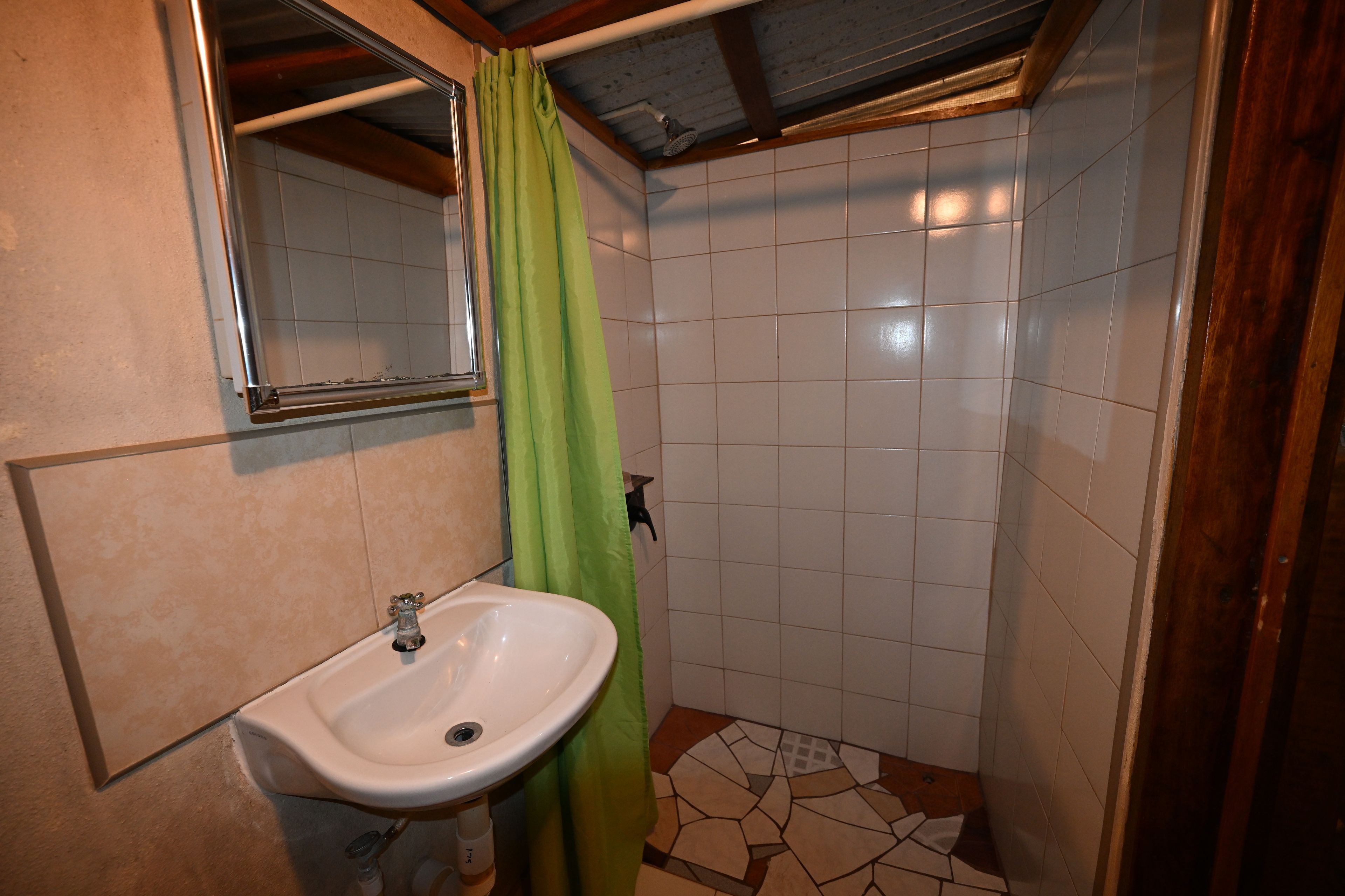 Une salle de bain avec un lavabo blanc, un rideau de douche vert et des murs carrelés.