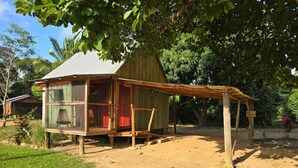 Una estructura rústica de madera con cerramiento de vidrio, una puerta roja y un tejado de paja.