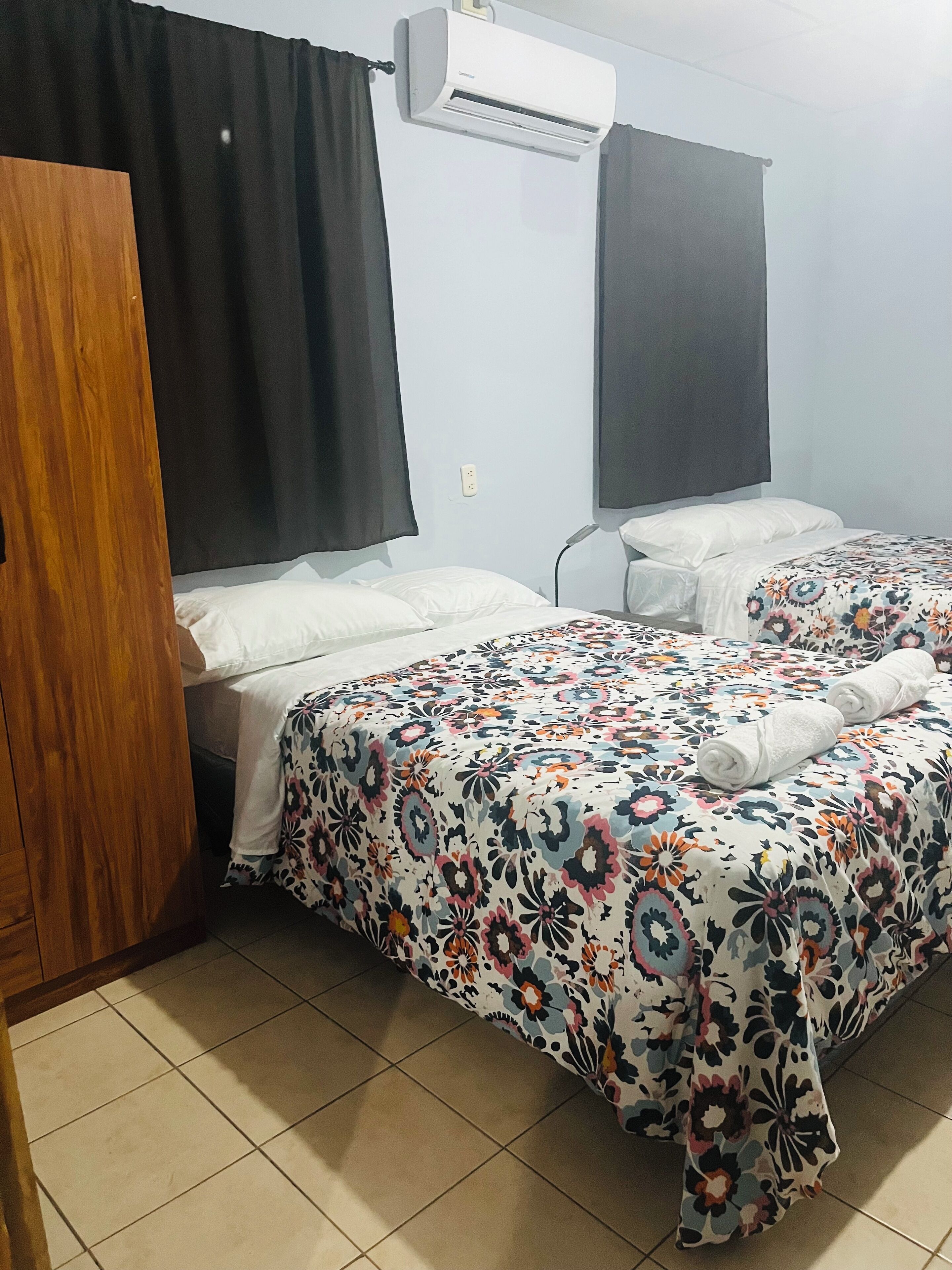 Une chambre à coucher comprenant un lit, une chaise, un appareil de climatisation et une armoire en bois.