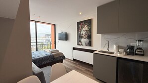A modern hotel room with a balcony, a kitchenette, and a dining area.