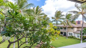 A residential area with a well-maintained lawn, palm trees, and a two-story house with a balcony.