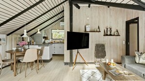A spacious living area with a high ceiling, a dining table with chairs, a sofa, a coffee table, and a flat-screen TV mounted on a tripod stand. - Beautiful home in Gedser with WiFi (Gedser)
