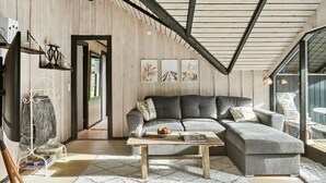 A cozy living room with a wooden ceiling, a grey sectional sofa, a coffee table, and a view of the outdoors. - Beautiful home in Gedser with WiFi (Gedser)
