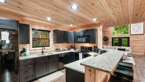 Una cocina moderna con armarios oscuros, encimeras de granito y techo de madera.