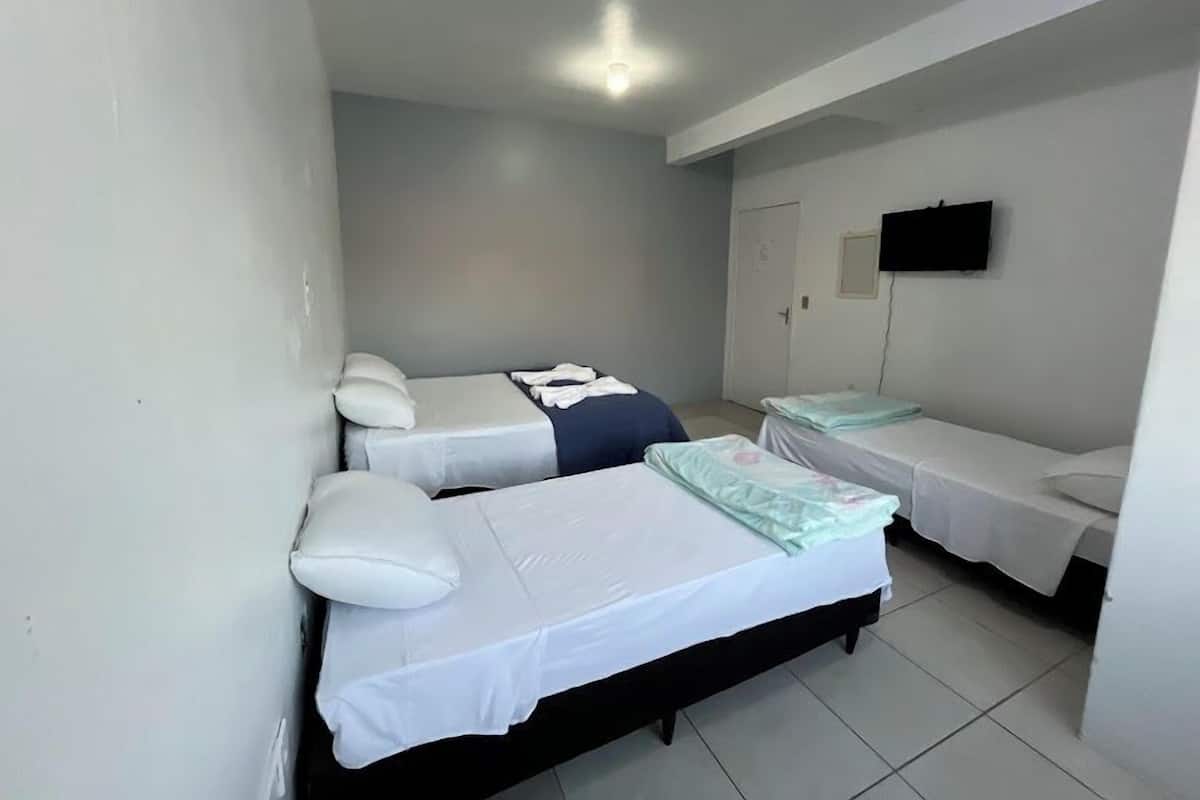 A small, clean room with two single beds, a flat-screen TV on the wall, and a door.