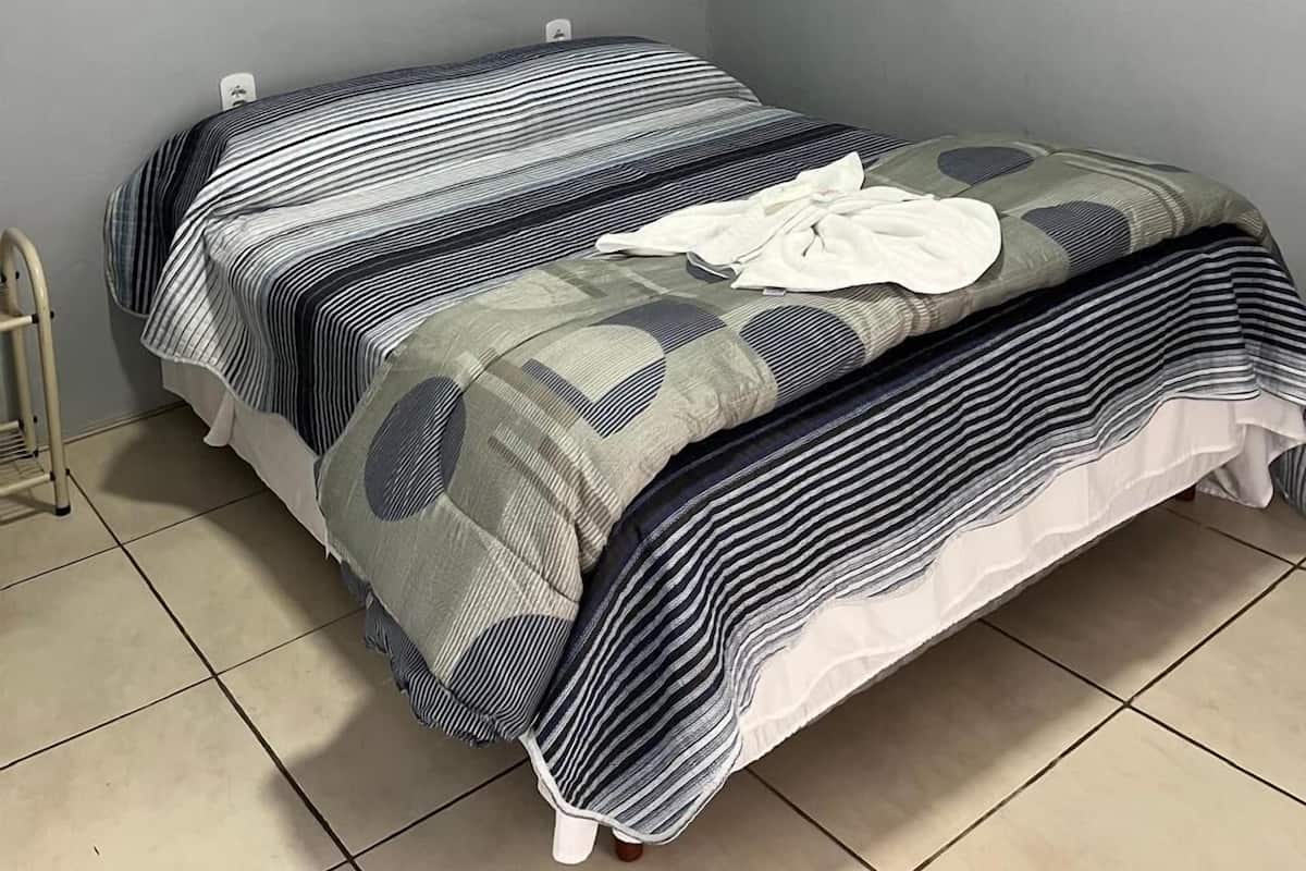 A single bed with striped bedding in a room with grey walls and tiled flooring.