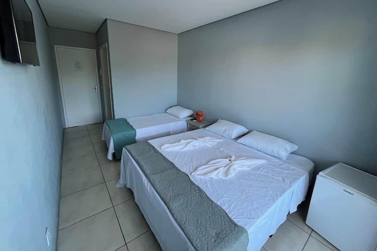 A hotel room with two beds, a small table, a refrigerator, and a TV on the wall.