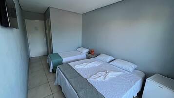 Habitación de hotel con dos camas, una mesita, un refrigerador y un televisor en la pared.
