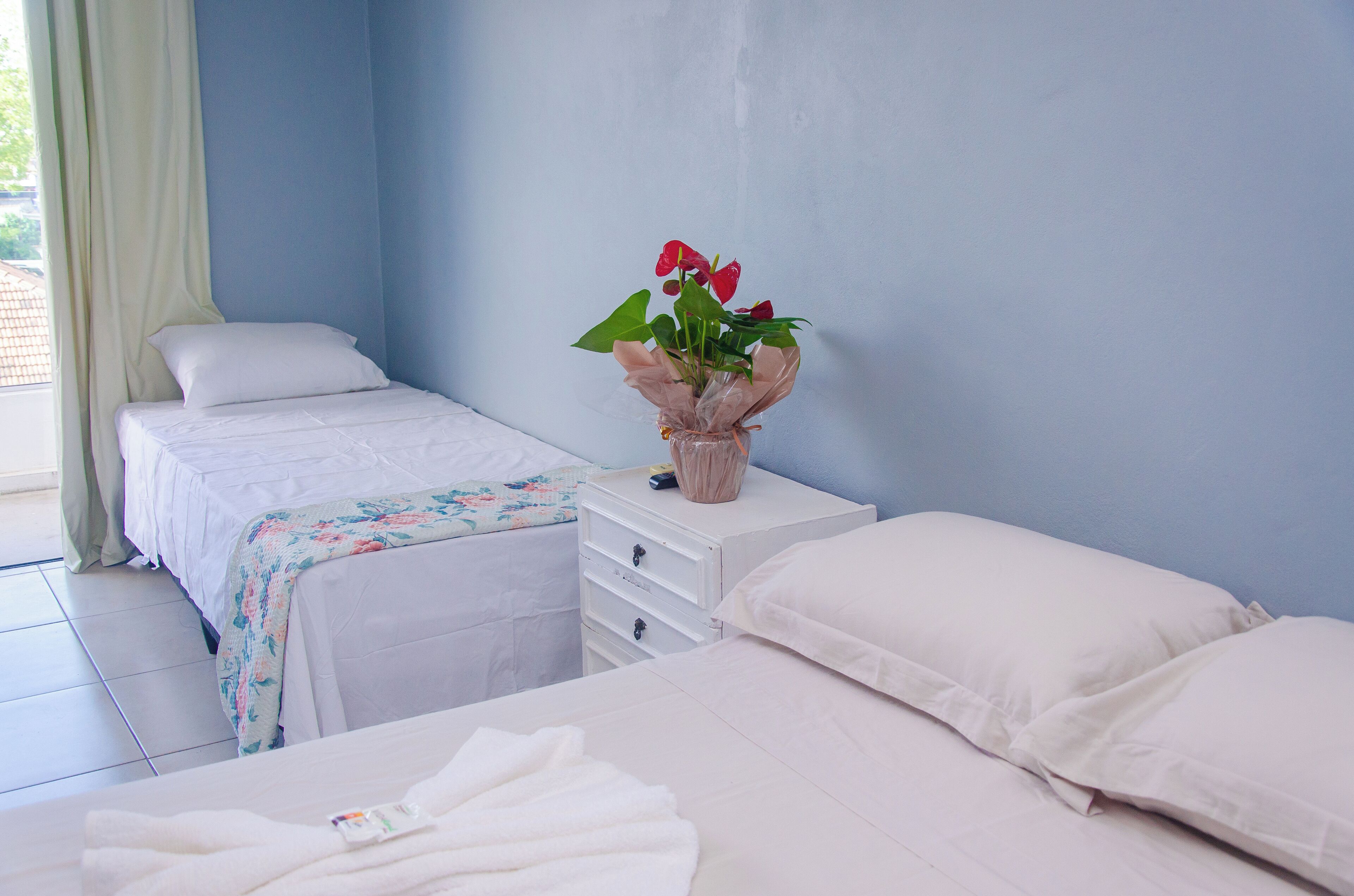 Habitació d'hotel amb dos llits, una tauleta de nit amb un vas de flors i una finestra amb cortines.
