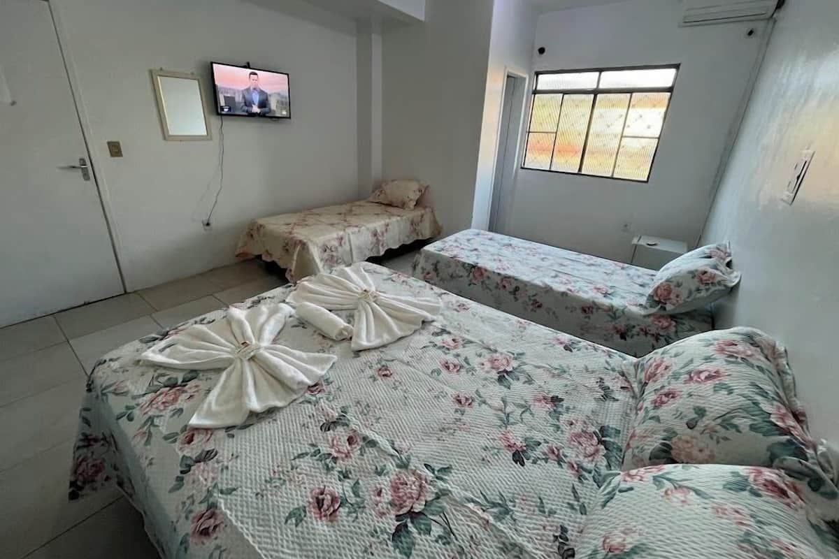 A hotel room with two single beds, a television mounted on the wall, and a window providing natural light.