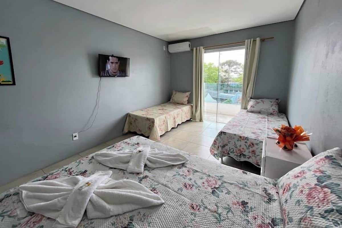 A hotel room with two beds, a TV, and a balcony with curtains.