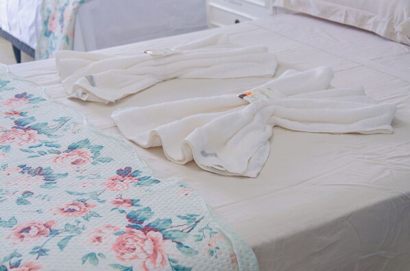 A neatly made bed with a floral-patterned blanket and two folded white towels. - Hotel Caçula Do pampa (Sao Gabriel)