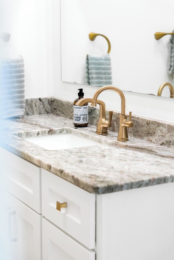 A bathroom with a marble countertop, gold faucets, and a soap dispenser. - The Winona Lake Chalet 1 (Winona Lake)