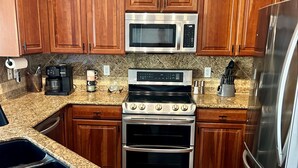 A kitchen with wooden cabinets, a stainless steel microwave, a coffee maker, a stove, and a refrigerator.